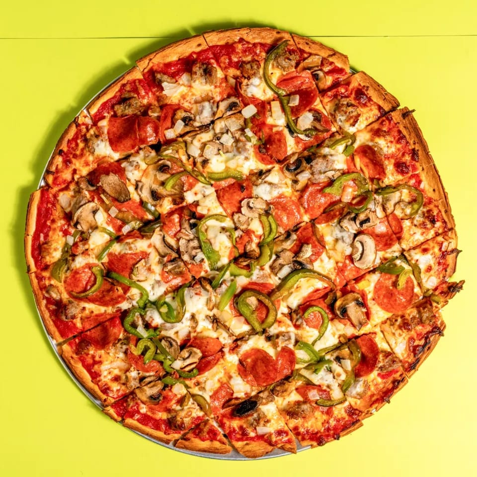 A whole pizza with pepperoni, sausage, mushrooms, onions, and green peppers on a yellow background.