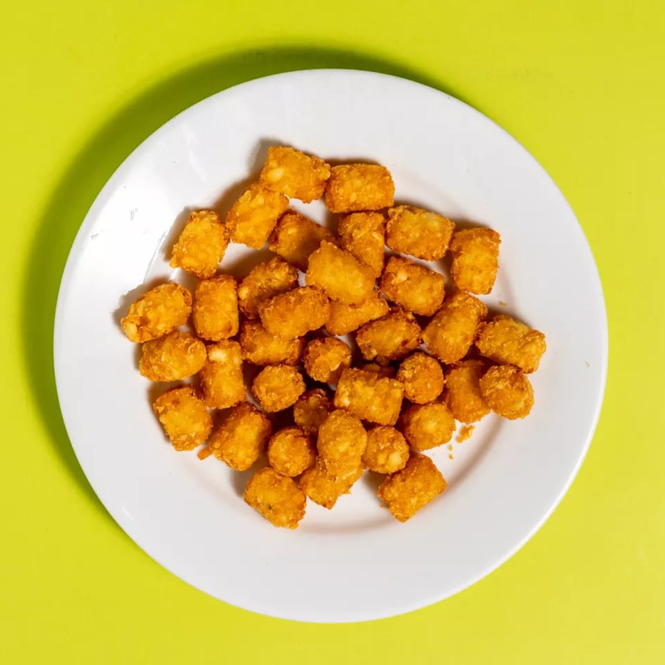 A white plate filled with golden-brown tater tots, set against a vibrant lime green background.