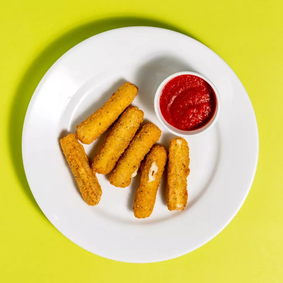 Golden-brown mozzarella sticks with marinara sauce on a white plate against a bright yellow background.