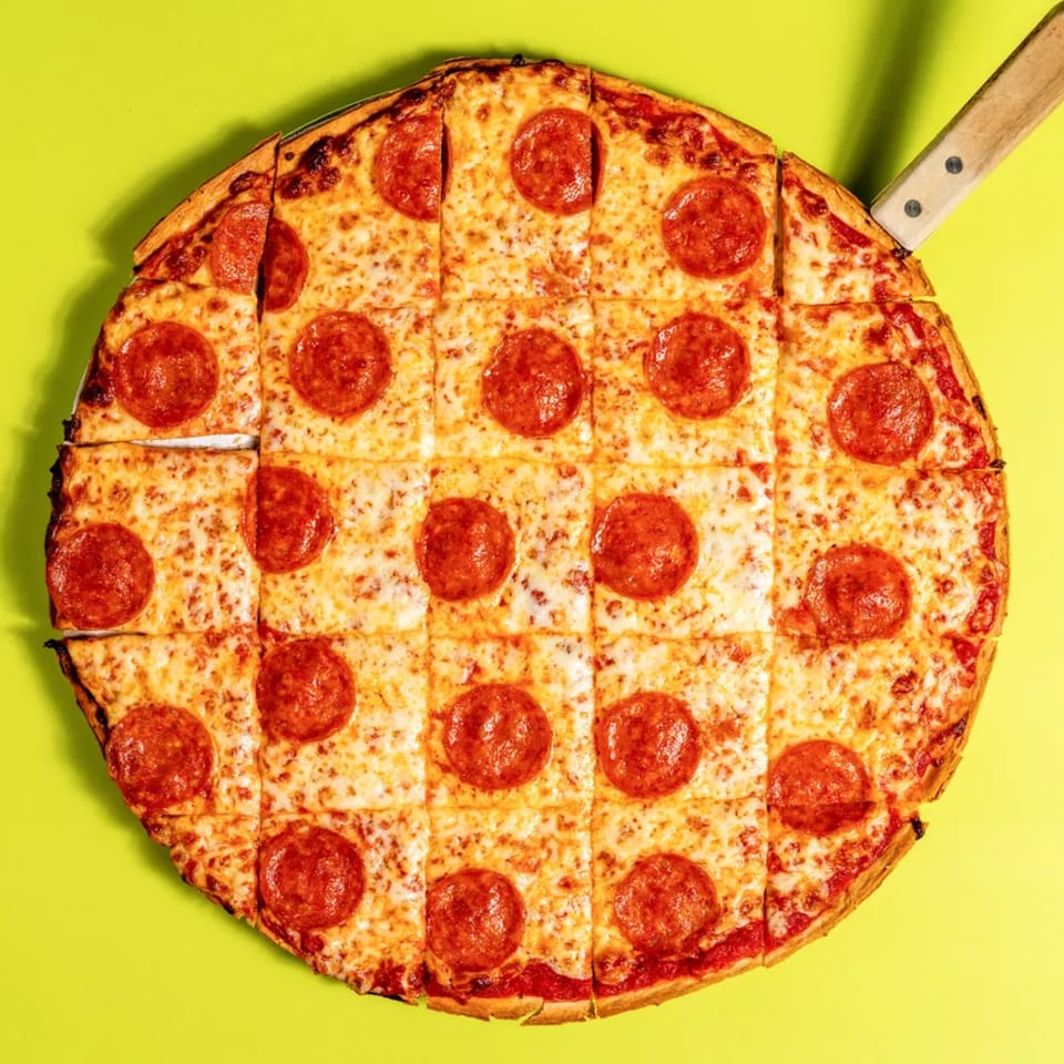 Square-cut pepperoni pizza with a knife handle visible on a bright yellow-green background.