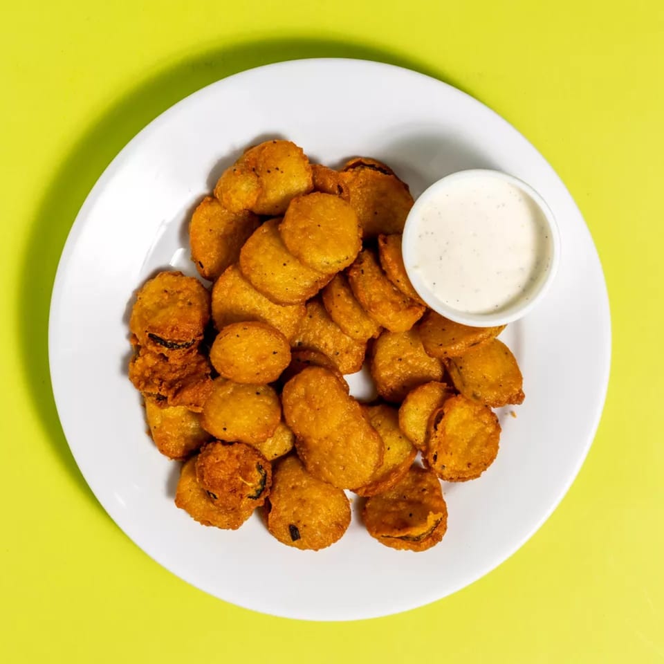 A white plate filled with golden-brown fried pickles and a side of creamy ranch dressing.